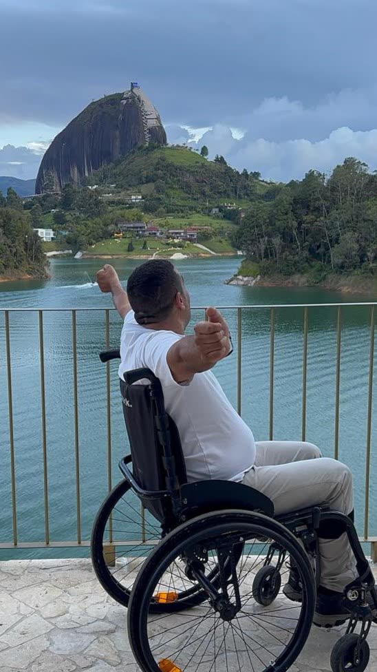 Un hombre en silla de ruedas abre los brazos frente a la represa de Guatapé